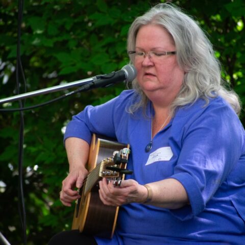 A musician plays a guitar and sings into a boom microphone